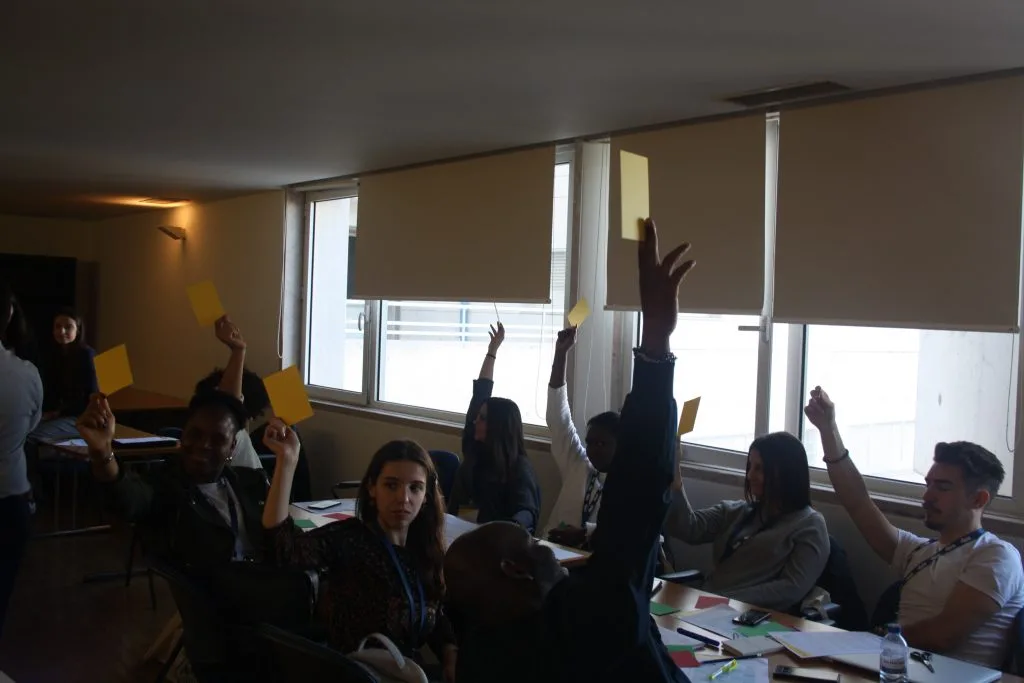 Participants seated around tables, each holding out a yellow card.