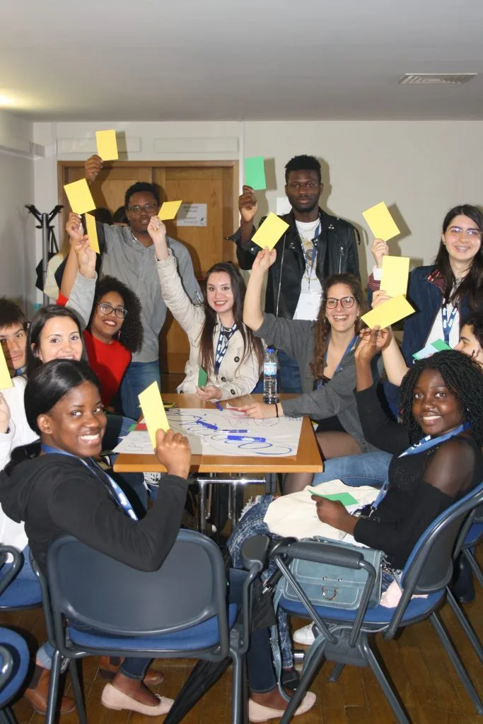 Participants seated around a table and some standing, each smiling while holding out a yellow card.
