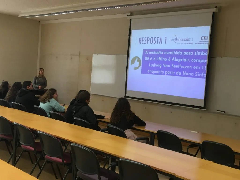 A larger view of the room with the CEI-IUL representative presenting the slideshow and six seated students listening.