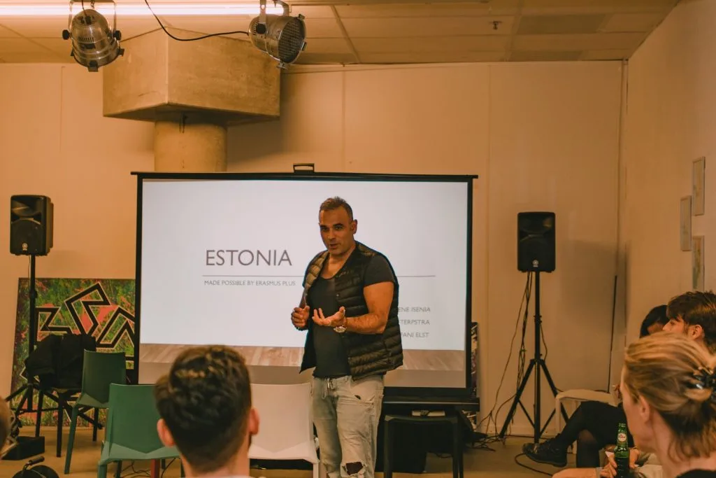 Man presenting, standing in front of projector panel showing a slideshow.