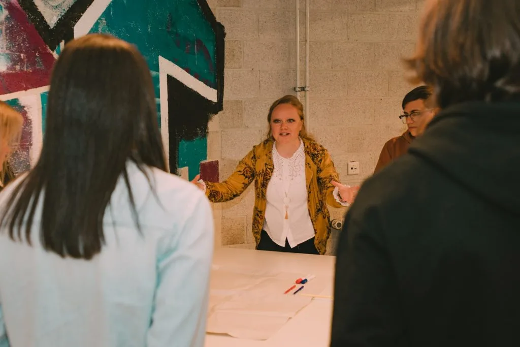 Participants around crafting table, woman speaking and three people listening.