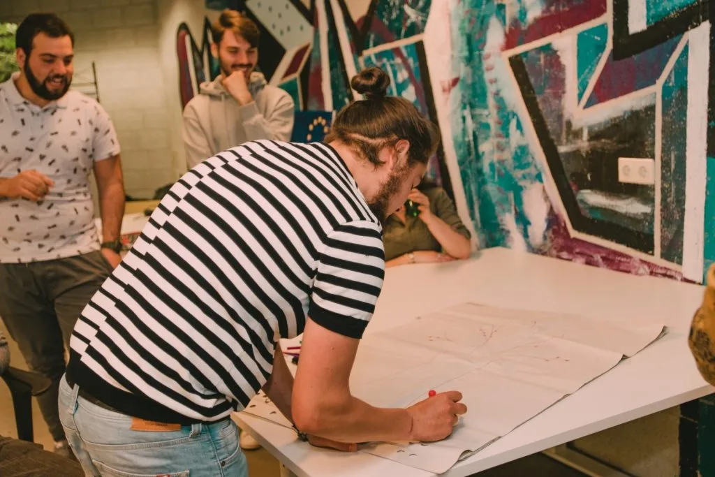 Man drawing on poster with two others watching.