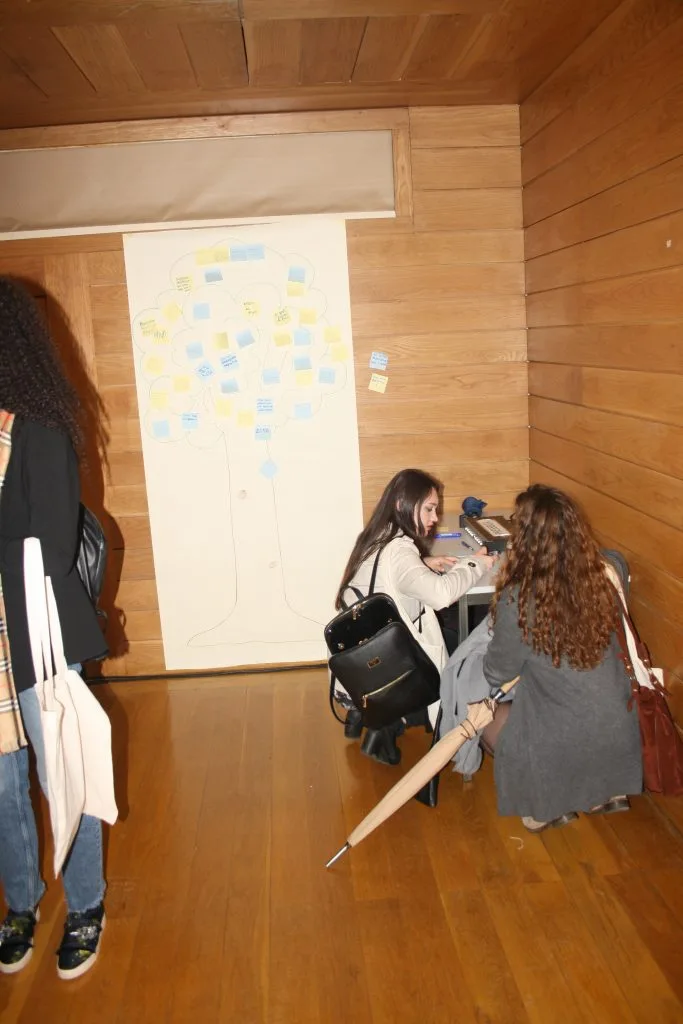 The "Tree of Europe" poster on a wall with three participants in front of it, one standing and two squatting near a table to write.