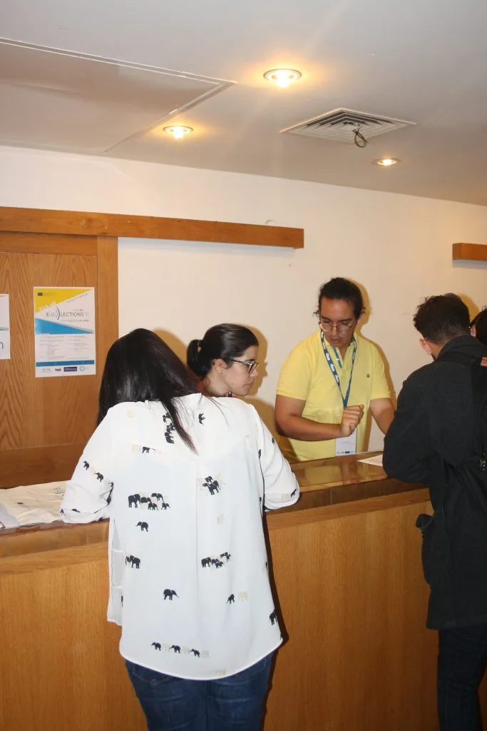 Participants signing in for the event, two persons bending over a counter with two others standing in the back of it.