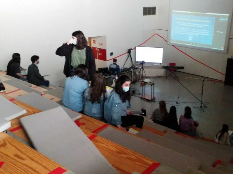 The students in the Arouca school auditorium organized in discussion groups, view from the back of the auditorium, with the projected videoconference in the front.