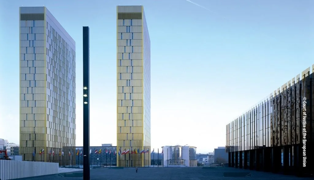 An outside view of the Court of Justice of the European Union, two tall buildings stand out over the blue sky.