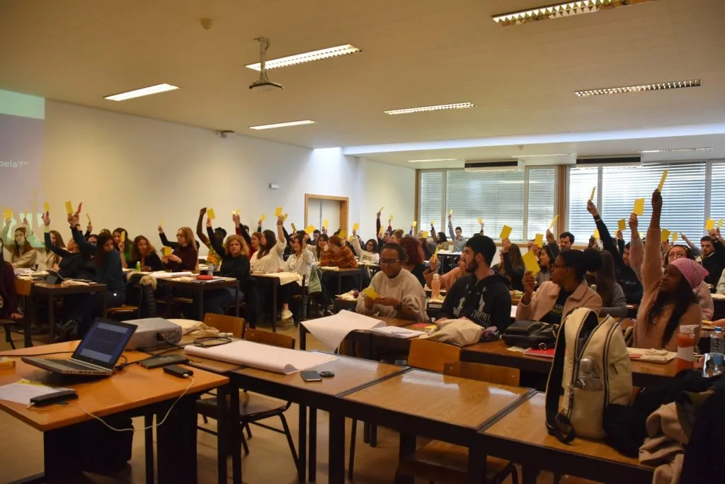 Classroom full of seated participants holding out mostly yellow cards, and some red ones.