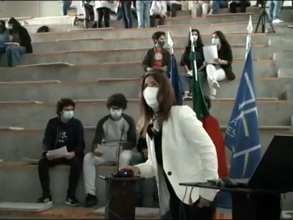 A teacher standing in front of the other students, using the videoconference equipment.