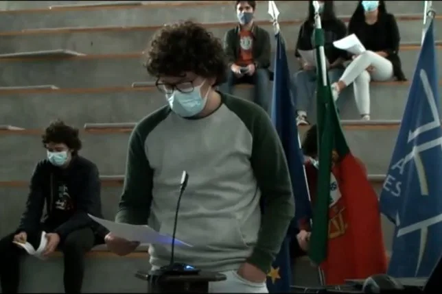 A student group representative standing in front of the other students, holding a paper while talking, sharing the conclusions of their group.