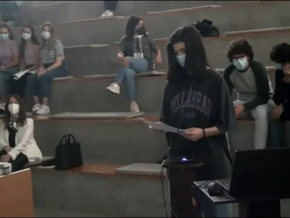 A student group representative standing in front of the other students, holding a paper while talking, sharing the conclusions of their group.