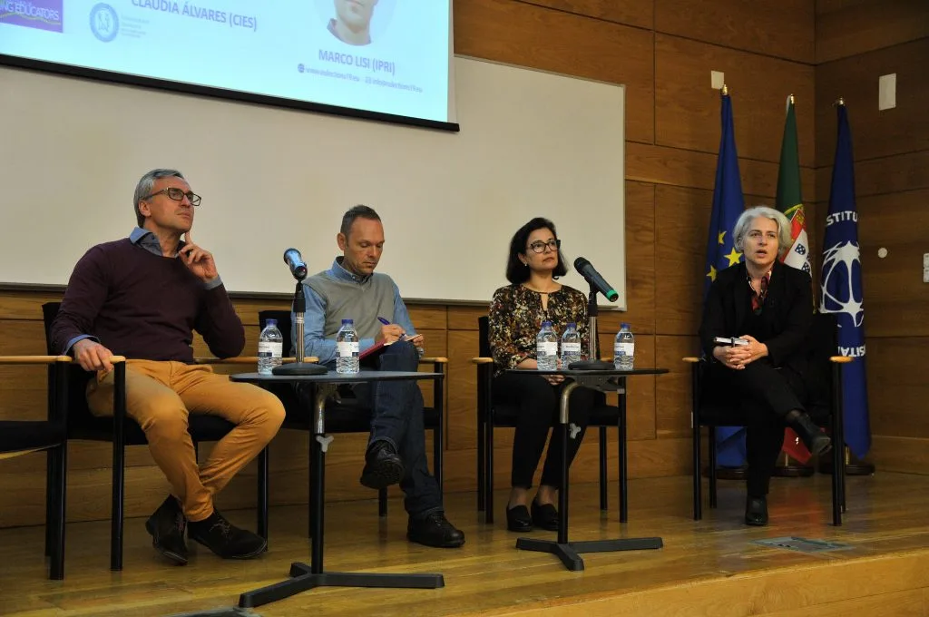Four roundtable participants seated on the auditorium stage during the event, with Catarina Carvalho talking.