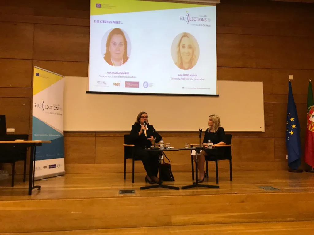 Ana Paula Zacarias and the hosting project coordinator seated on the auditorium's stage during the talk.