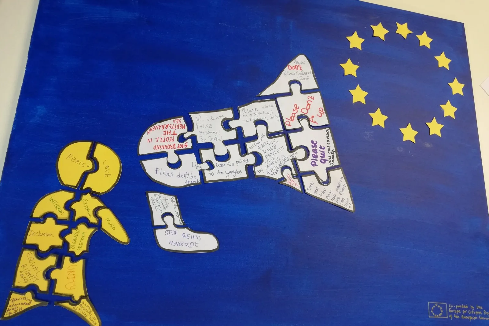 Participant-made poster - Human figure with megafone  made of diverse puzzle blocks of messages beside European Union star circle over blue background.