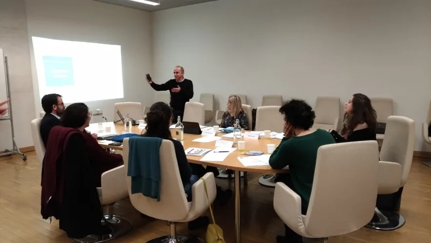 Representatives seated around a table paying attention to a projected presentation being done by a representative of CEI-IUL.
