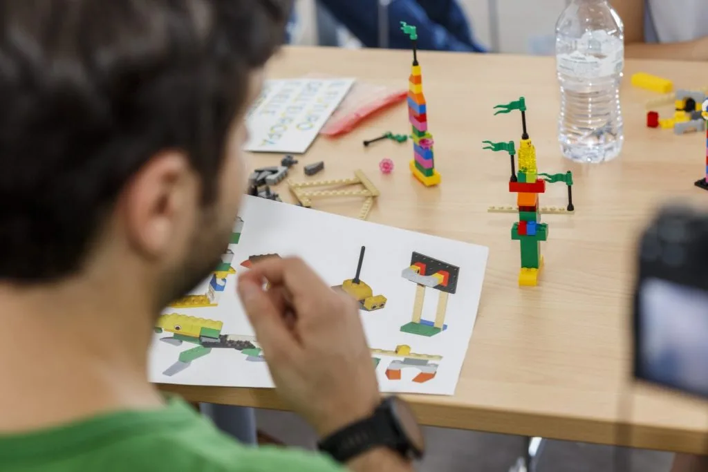 Participant holding an illustrative activity paper sheet with two Lego constructs on the table.