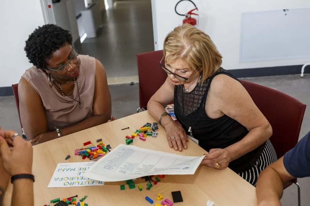 Two participants talking over the scenarios, one person holding the paper sheet while showing to the other.