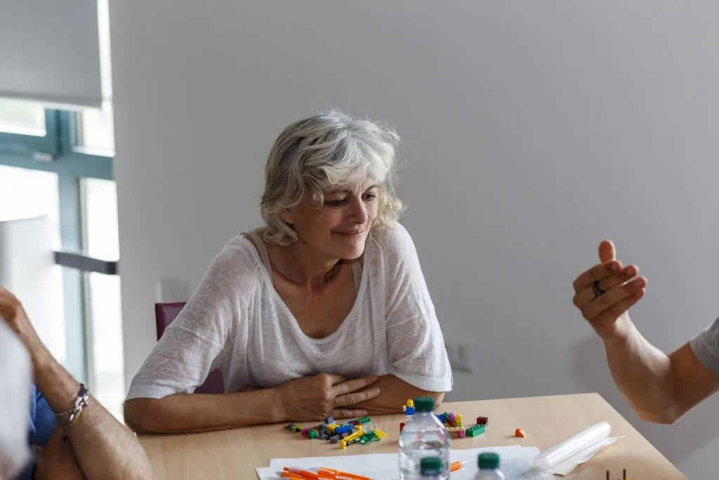 Participants talking over table with Lego pieces with woman listening at the center.