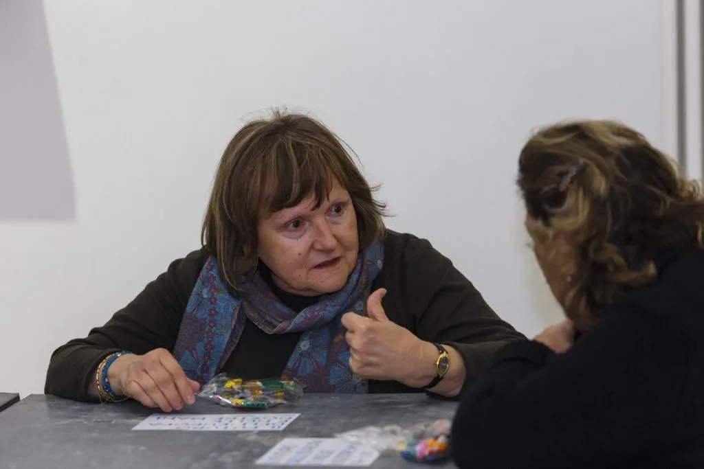 Two seated participants speaking to each other, with unopened bags of Lego pieces in front of them.